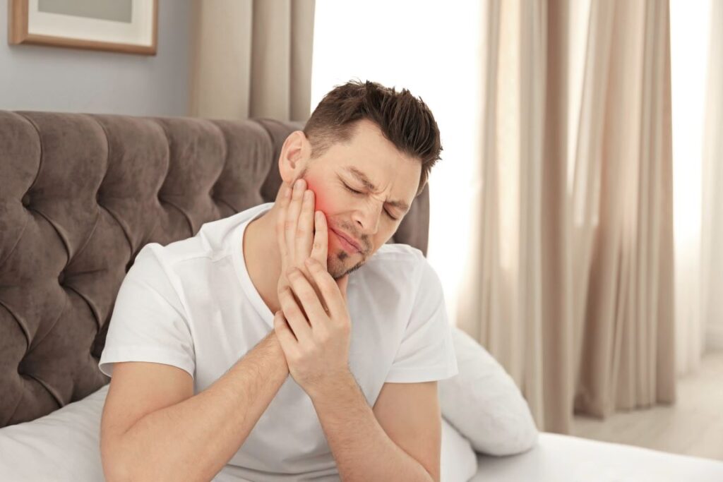 A man sitting in his bed with jaw pain.