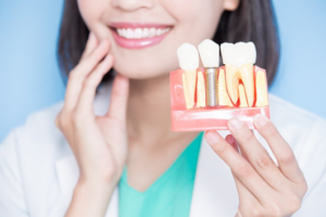 Dentist smiling and holding up a model of a dental implant